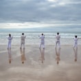 7 persons stands on beach facing sea
