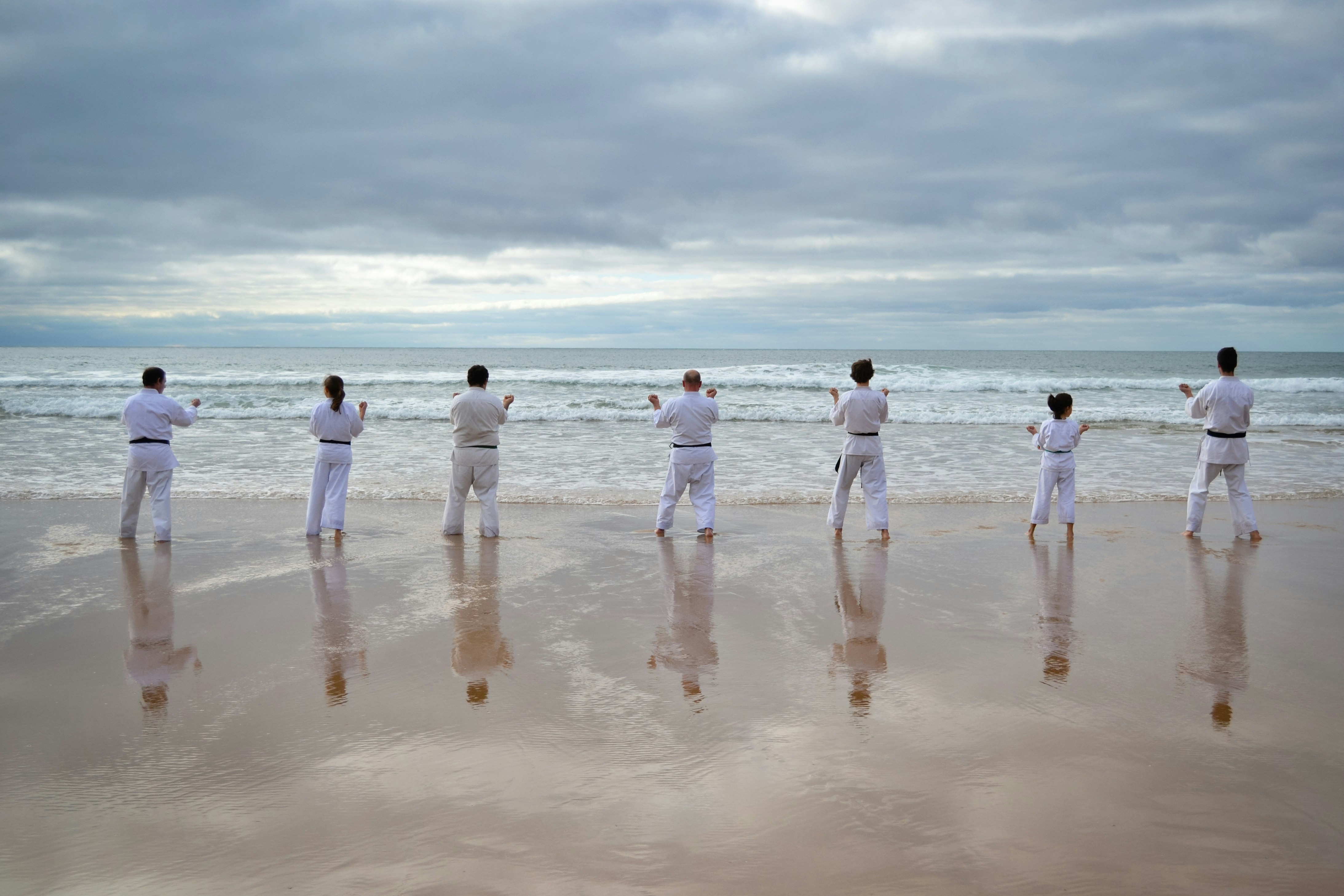 7 persons stands on beach facing sea