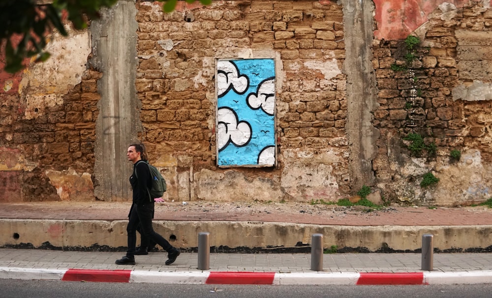 woman in black walks beside brown brick wall