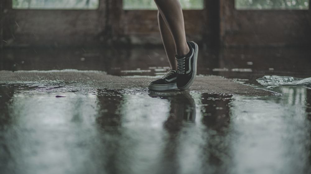 persona con zapatillas Vans negras caminando sobre pavimento mojado