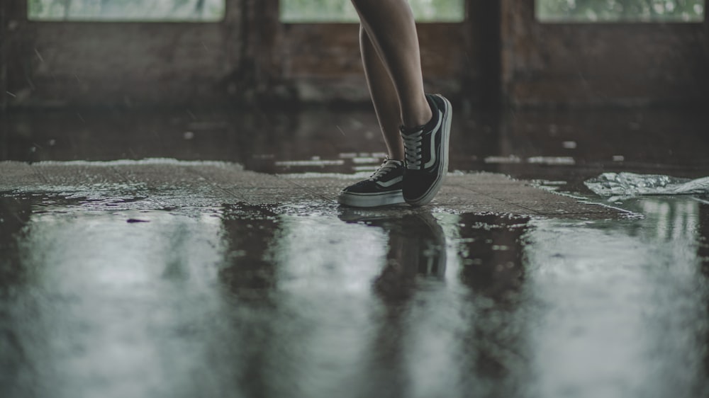 person with black Vans sneakers walking on wet pavement