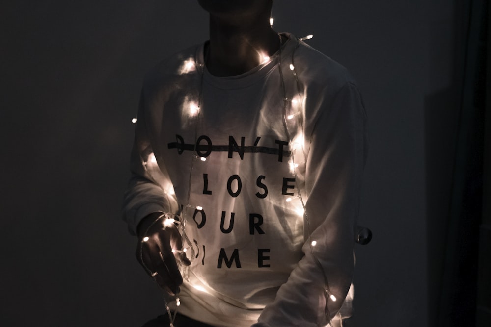 man in white sweater holds lighted Christmas light