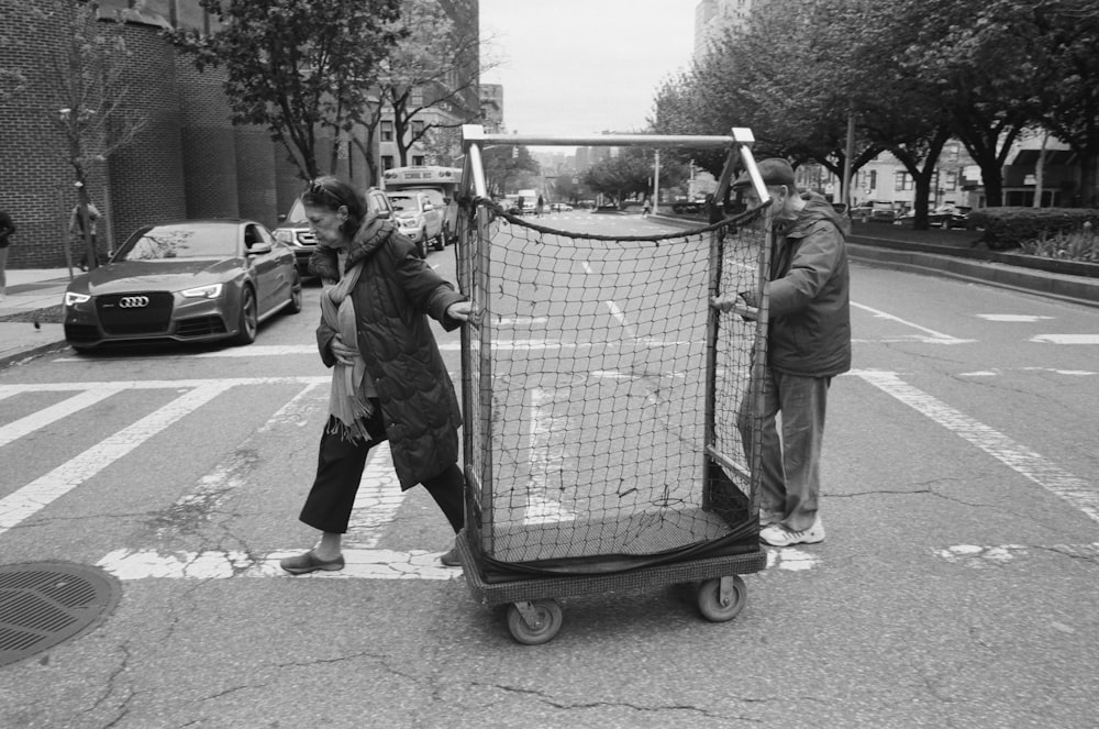 grayscale photo of couple with cart crossing street