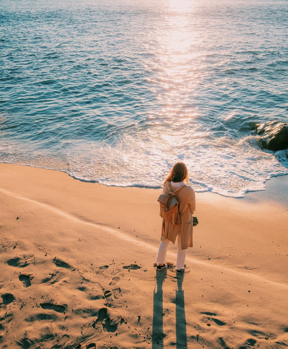 woman standing near shoreline during golden hour
