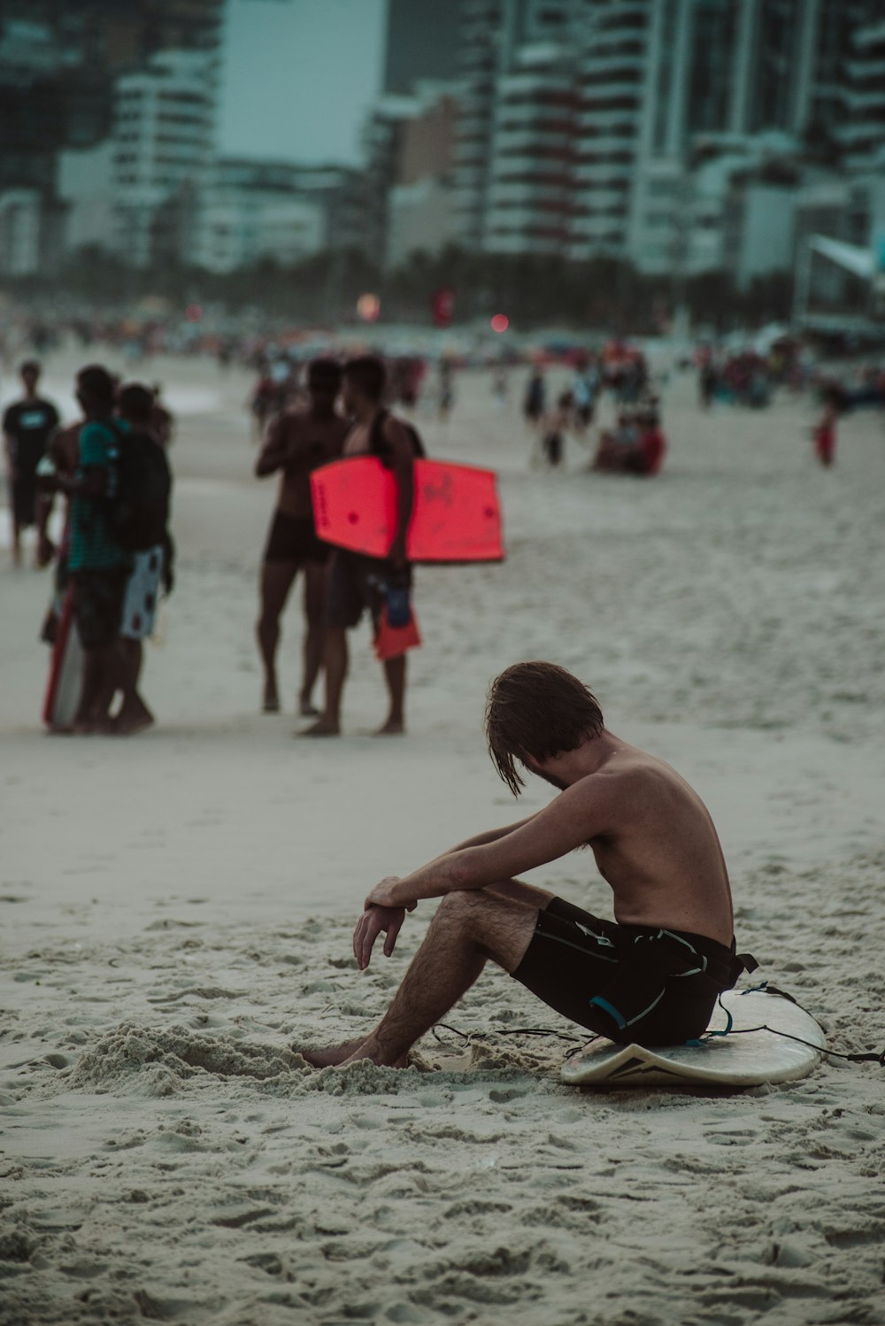 man sitting on white surfboard on sand during daytime