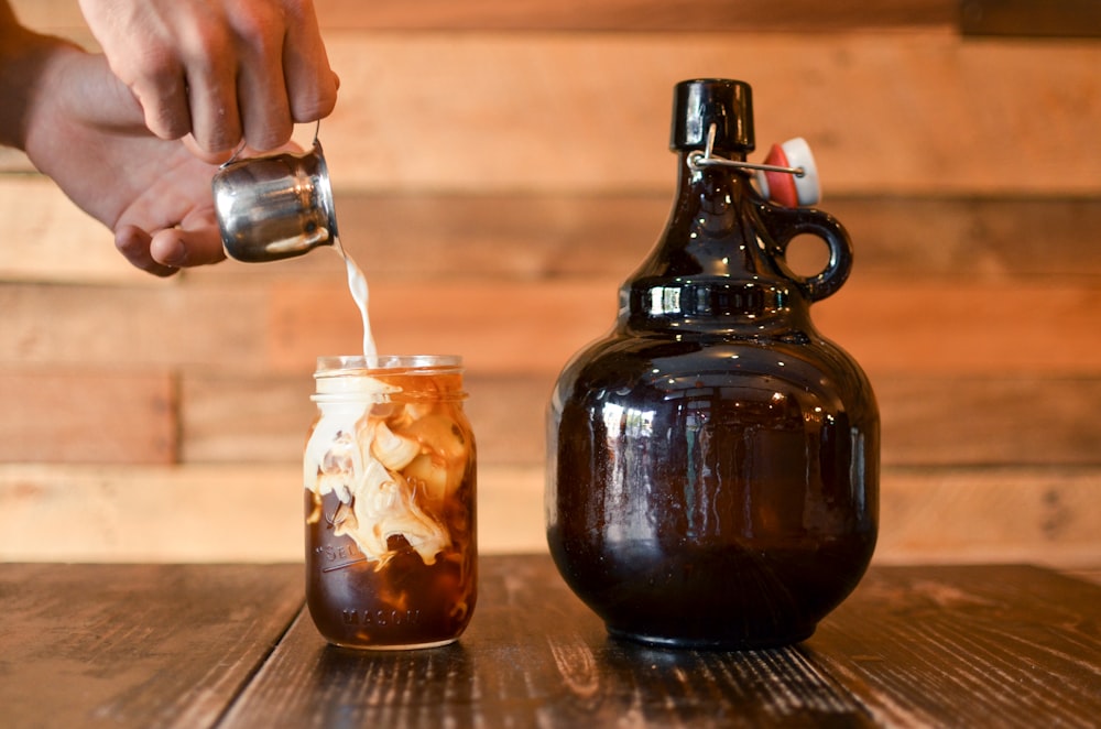 person pouring milk on mason jar