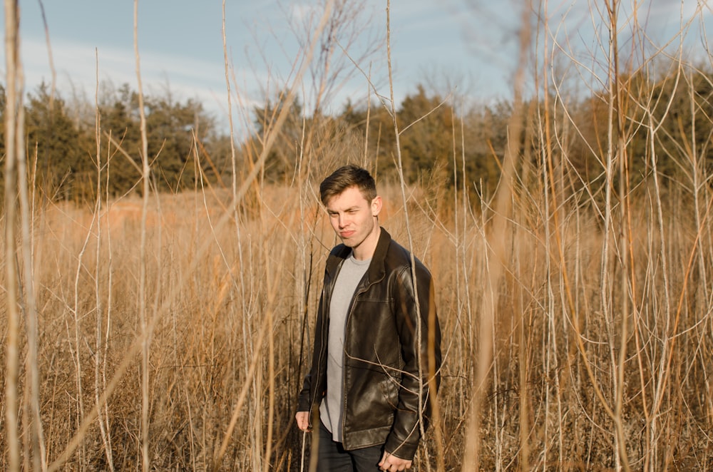 man wearing black leather jacket standing surrounded by brown grass