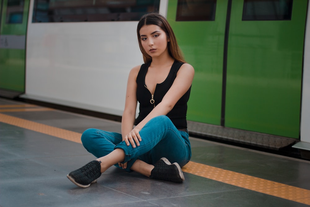 Mujer con blusa negra sin mangas y jeans azules sentada en el camino del túnel del tren