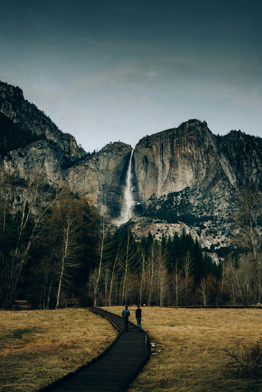 two men walks on footbridge through waterfalls