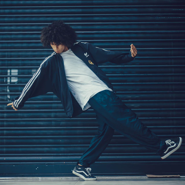 A dancer in a grey tracksuit posing in front of a black metal roll up door in Tunis