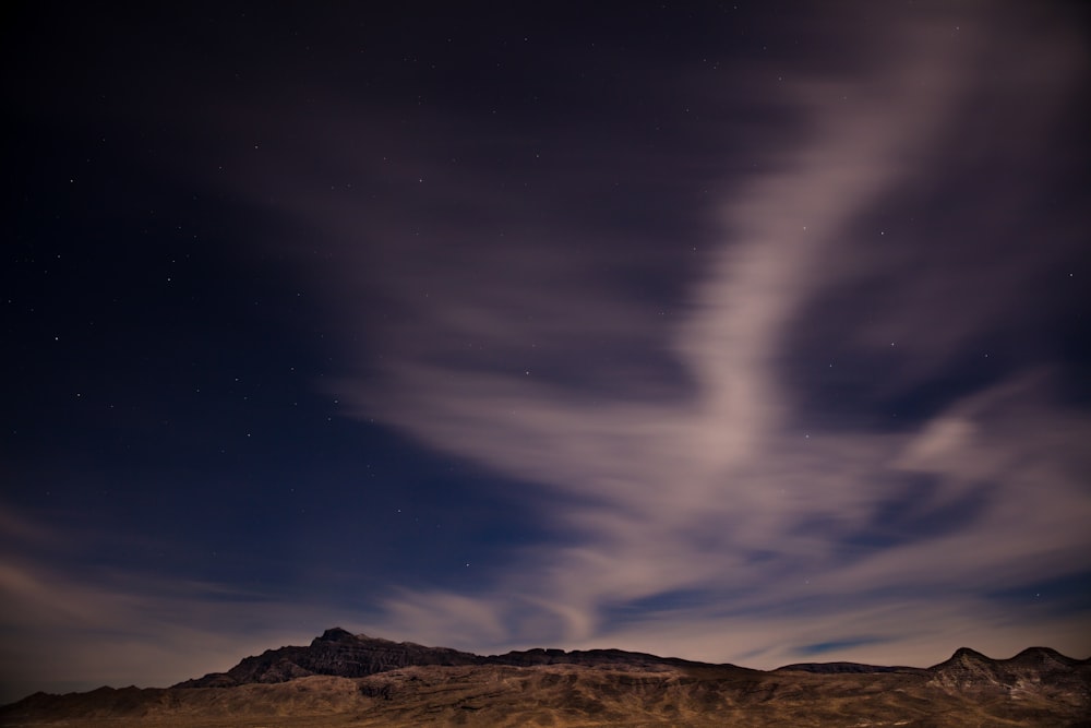 brown mountain under blue and white skies