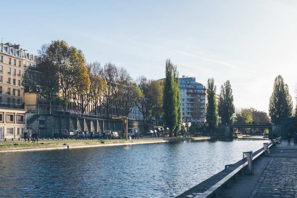 Menschen, die in der Nähe der Straße spazieren gehen, umgeben von Gebäuden und Bäumen, die einen ruhigen See sehen