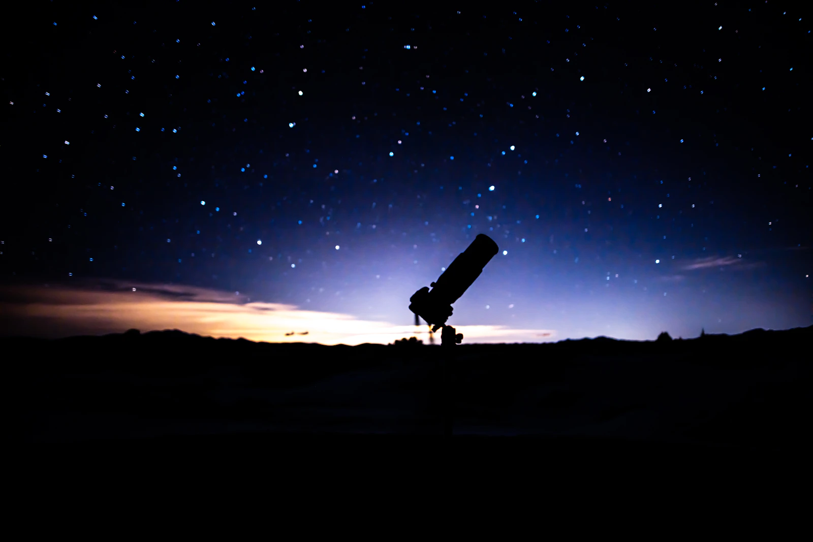 A telescope on a hilltop beneath a star-filled night sky
