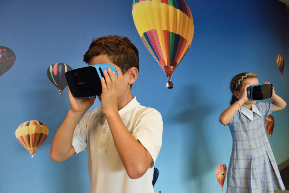 소년과 소녀는 뜨거운 공기 풍선 벽지 앞에서 VR 고글을 사용합니다.