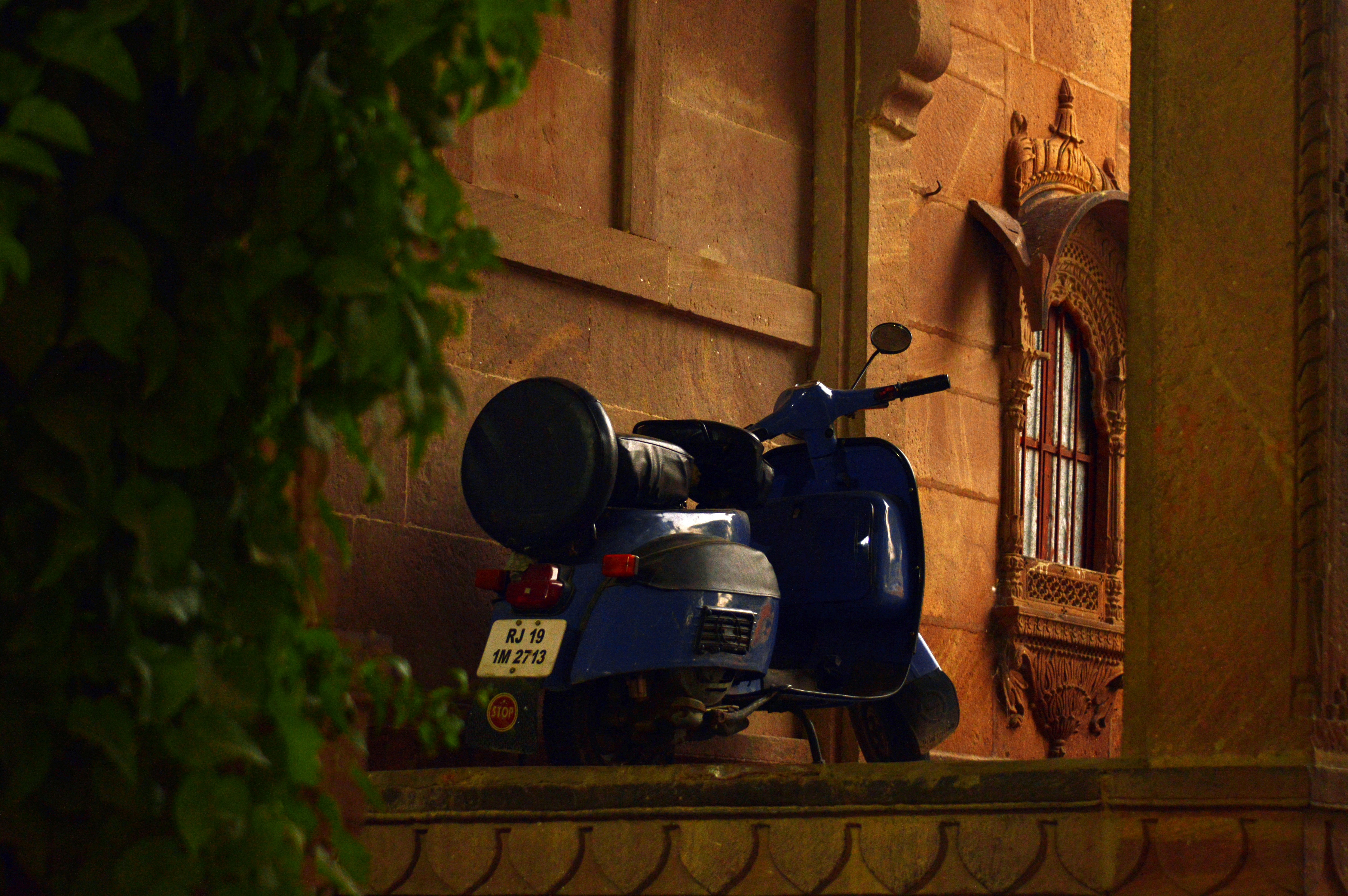 blue motor scooter parked beside building