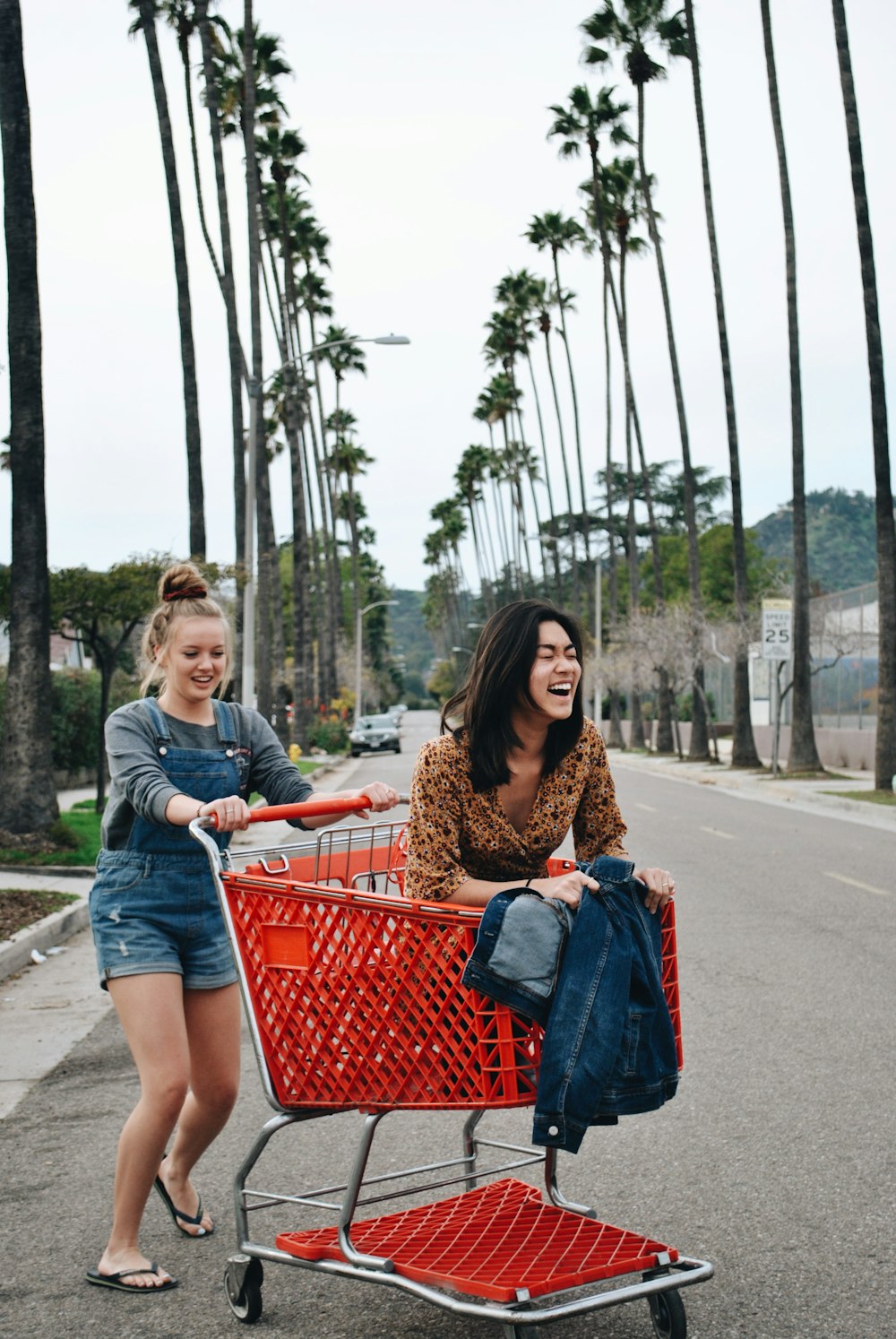 woman riding shopping cart with another woman pushing it in the middle of road