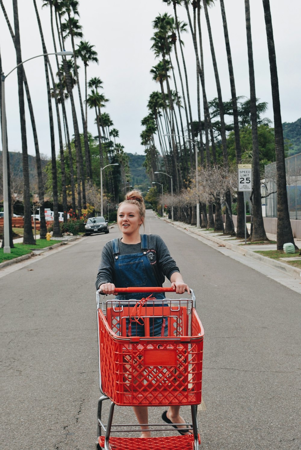 woman in blue shirt holding red cart in middle of road