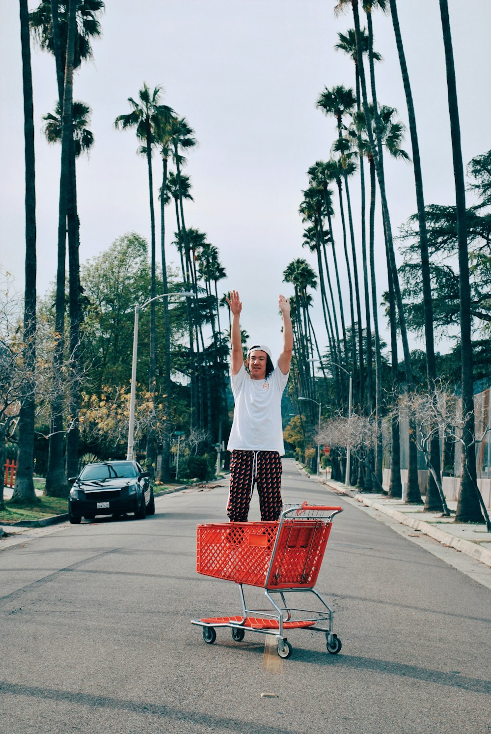 man stands in red shopping cart at the street