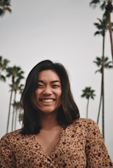 A candid photo of Kira smiling outdoors with palm trees and a sunny California sky in the background.