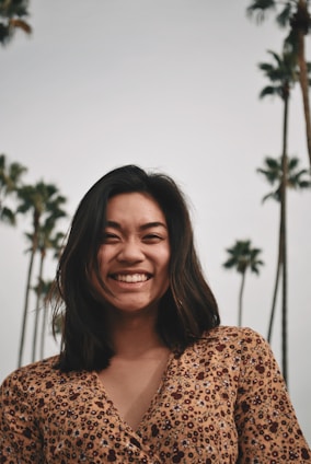 A candid photo of Kira smiling outdoors with palm trees and a sunny California sky in the background.