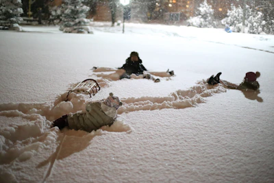 Children bundled up in colorful coats making snow angels on a fresh blanket of snow.