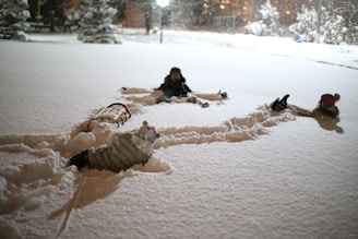 The three kids bundled up in bright jackets, making snow angels under a clear blue sky.