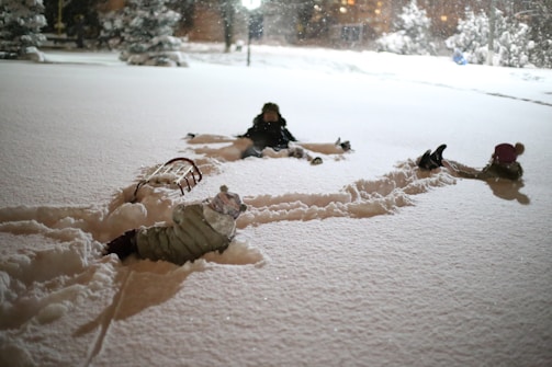 The three kids bundled up in bright jackets, making snow angels under a clear blue sky.