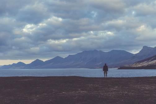 Wide shot of a lone figure standing against a vast, dark landscape.