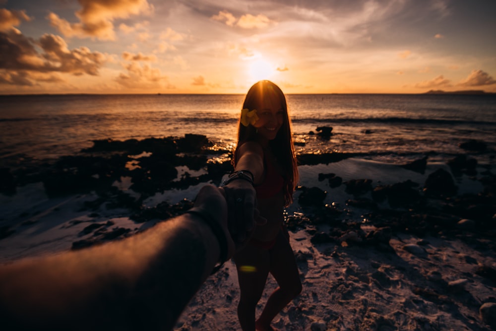 mulher segurando a mão da pessoa andando na praia com vista do pôr do sol