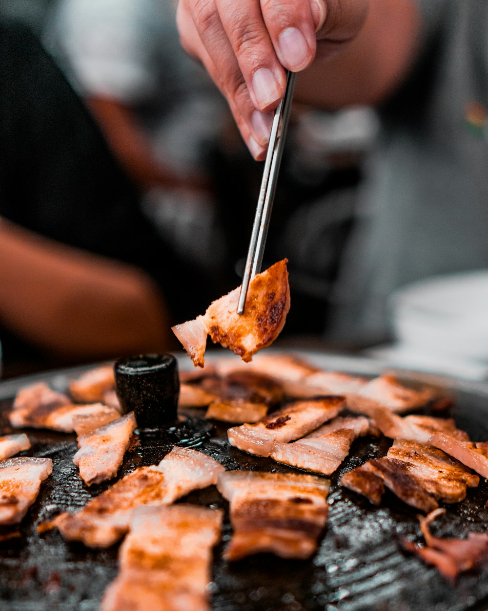 person picking grilled meat from grill using sticks