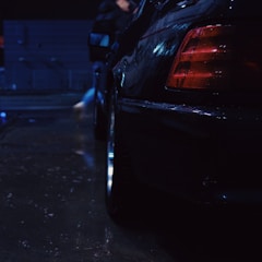 Close-up of a sleek black car wrapped in glossy hentair film under city lights.