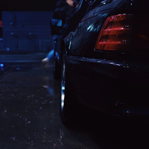 Close-up of a black Ford Mustang front splitter with subtle red accents under moody urban lighting