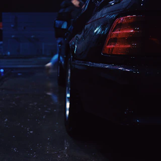 Close-up of a black Ford Mustang front splitter with subtle red accents under moody urban lighting