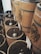 Large wooden barrels filled with dark roasted coffee beans are lined up, each with a metal scoop resting on top. The barrels are branded with a logo, and labels are attached, possibly indicating different types of coffee.