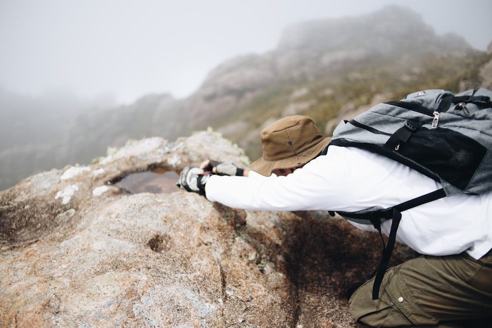 man climbing on brown mountain while carrying backpack