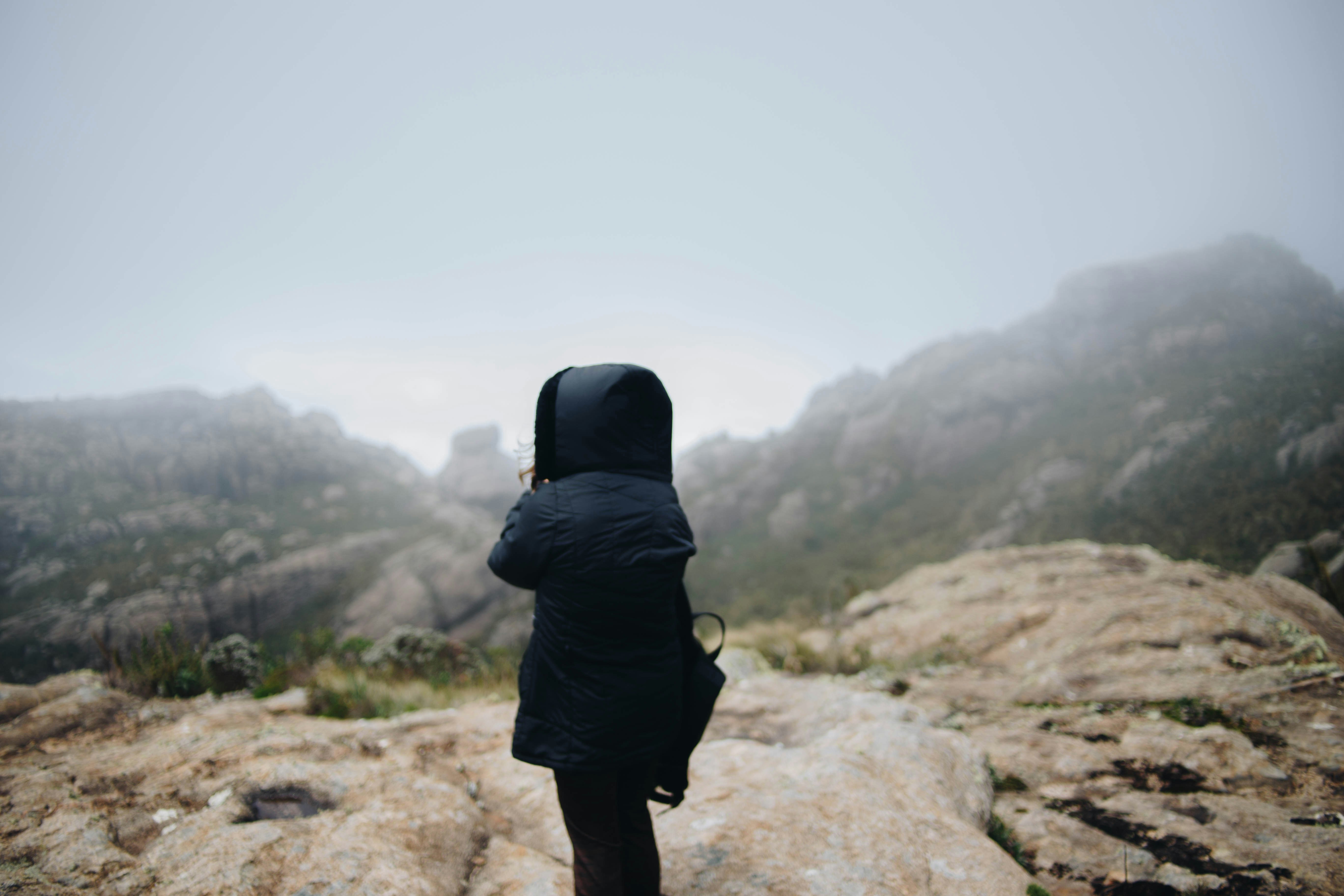 person wearing black hoodie bubble jacket standing on mountain