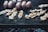 Shrimp skewers and several sausages are grilling over a charcoal barbecue. The skewers are neatly arranged, showcasing their grilled texture, with bits of seasoning visible. The metal grill grates are blackened from use, and there is a soft focus on the smoky background.