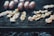 Shrimp skewers and several sausages are grilling over a charcoal barbecue. The skewers are neatly arranged, showcasing their grilled texture, with bits of seasoning visible. The metal grill grates are blackened from use, and there is a soft focus on the smoky background.