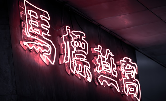 Bright pink neon Chinese characters illuminated against a dark wall, creating a glowing effect. The light reflects softly on the surrounding surfaces, emphasizing the vibrant lettering.