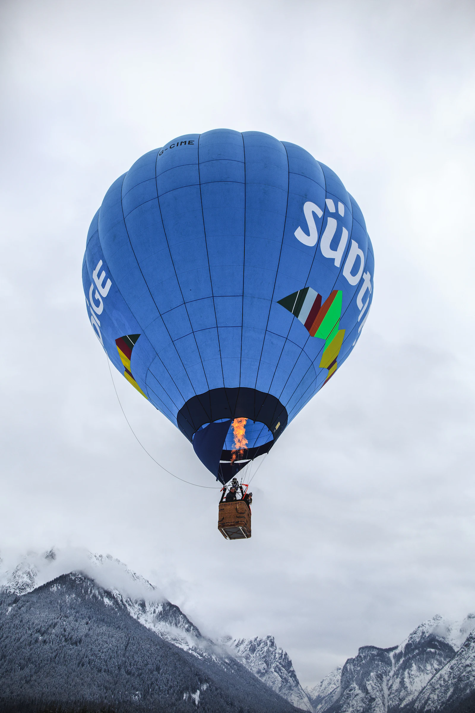 Montgolfière bleue et blanche au-dessus de montagnes enneigées (image d'illustration)