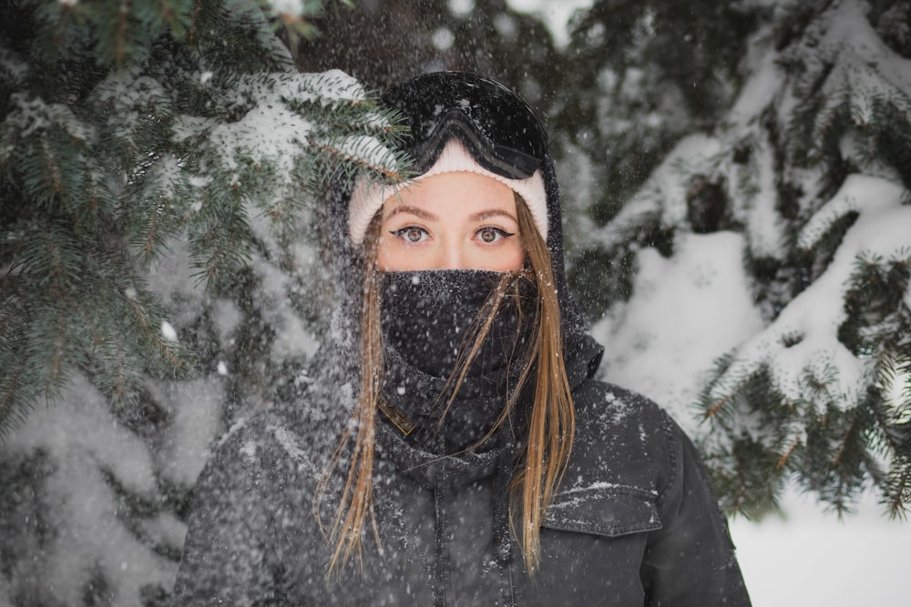 mujer con máscara de pie junto a un pino cubierto de nieve