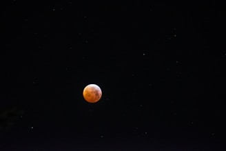 A glowing red moon, possibly representing a lunar eclipse or blood moon, set against a dark, starry night sky.