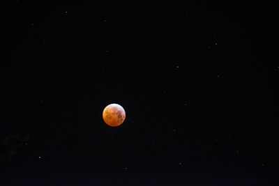 A glowing red moon, possibly representing a lunar eclipse or blood moon, set against a dark, starry night sky.