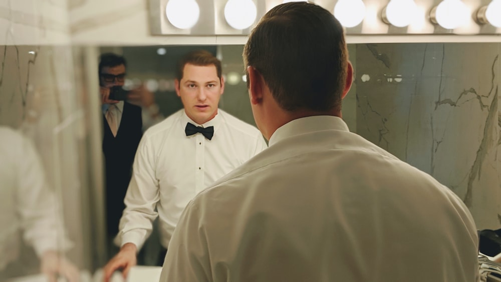 man wearing white dress shirt and black bowtie facing vanity mirror