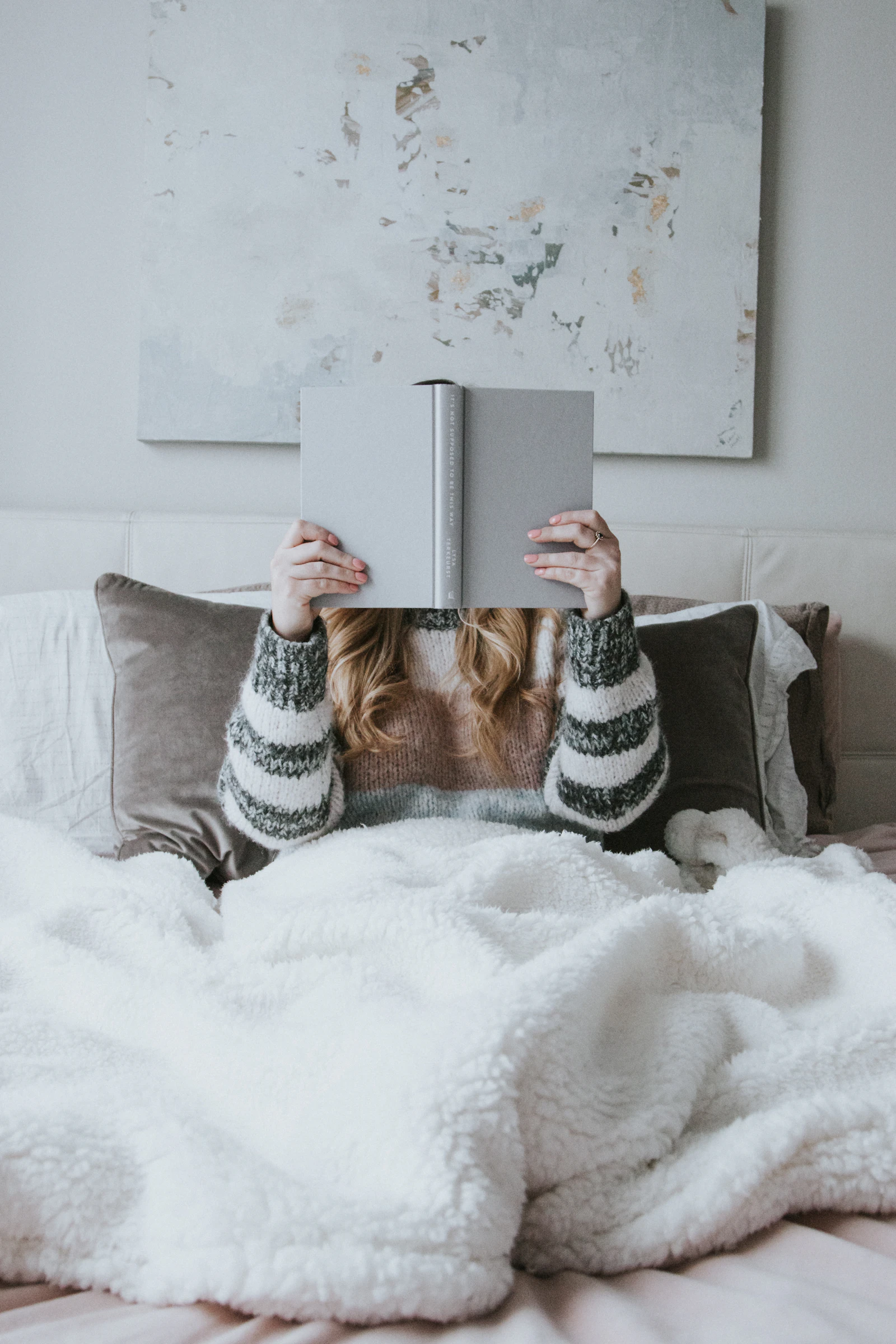Femme allongée sous une couverture moelleuse, tenant un livre ouvert devant elle