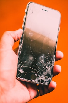 A close-up of a hand holding a smartphone with a cracked screen.