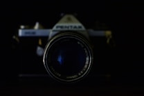 A vintage camera with a prominent lens takes center focus against a dark background. The branding and text around the lens are visible, adding a nostalgic touch.