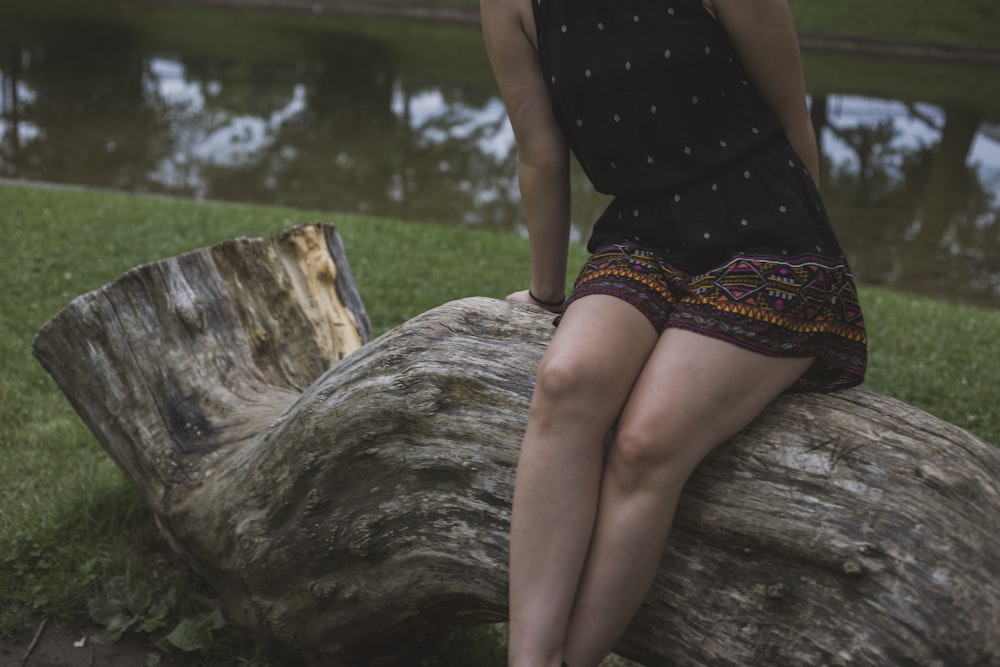 woman sitting on wood log near body of water