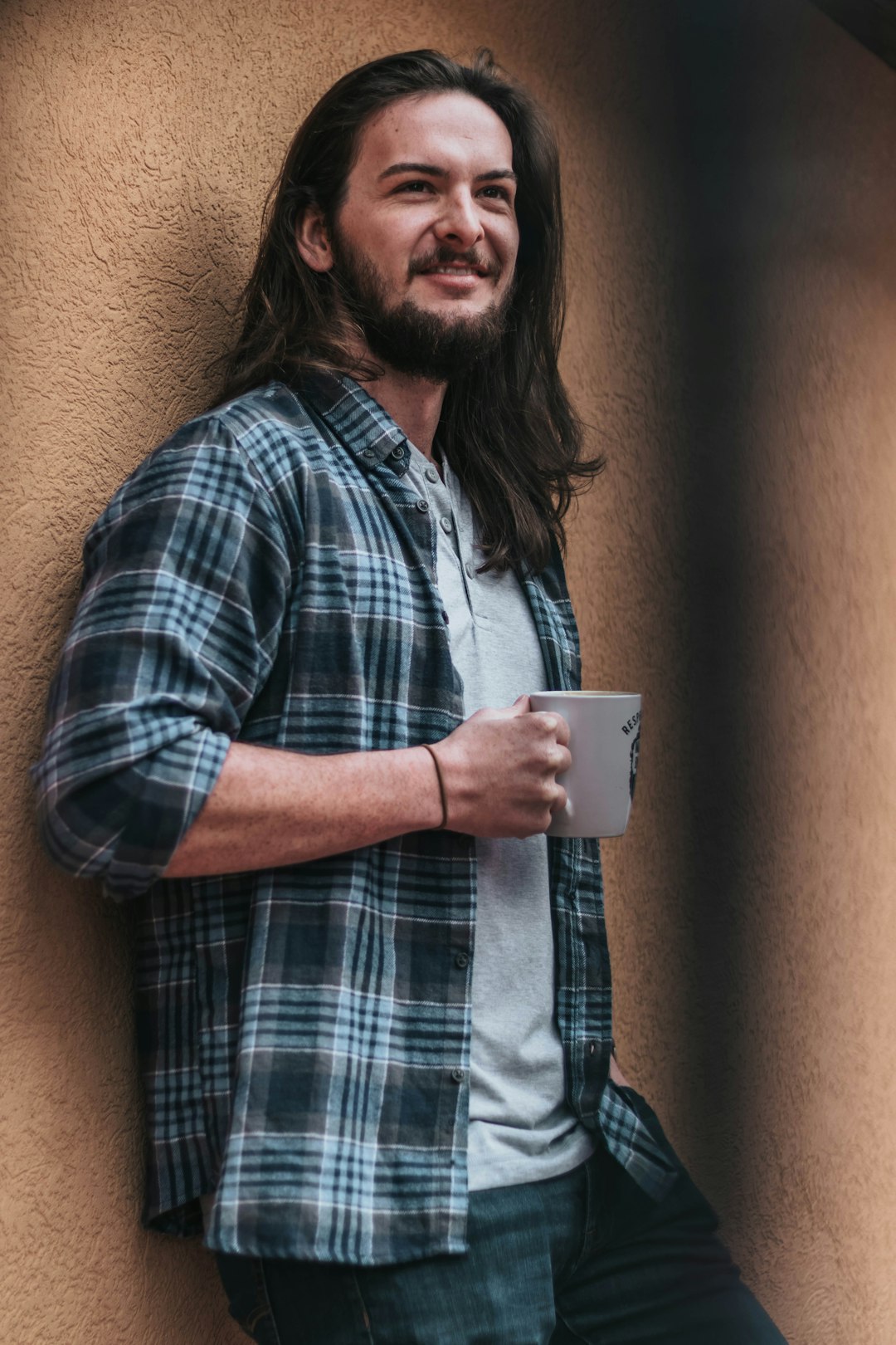 man holding mug leaning on wall