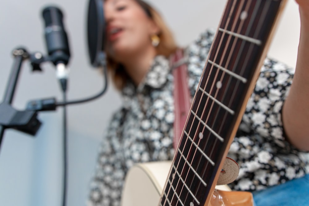 Femme jouant de la guitare acoustique tout en chantant à l’aide d’un microphone à condensateur